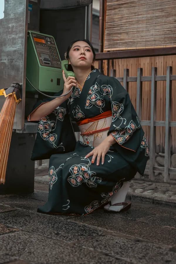 Una mujer con kimono japonés tradicional agachada ante un teléfono público verde en una calle de Japón