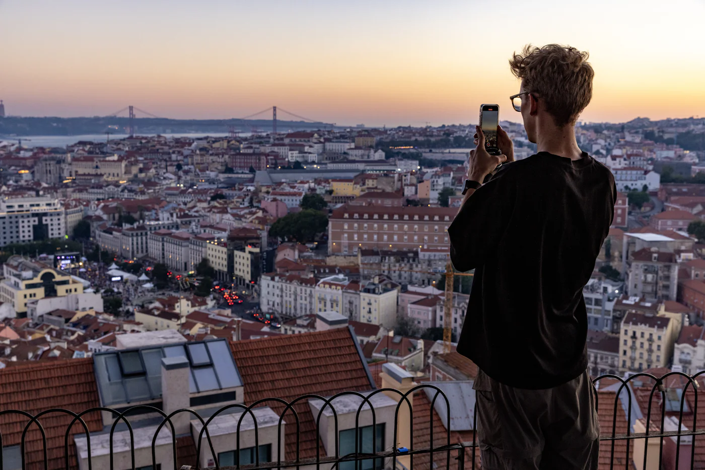 Traveler using his phone above the rooftops of a European city at sunset