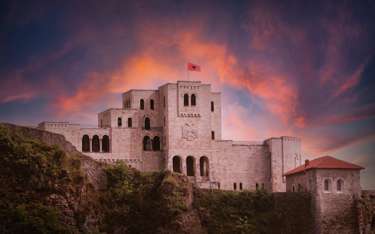 El castillo de Kruja sobre el pueblo, en Albania, al atardecer, con la bandera albanesa ondeando en la torre