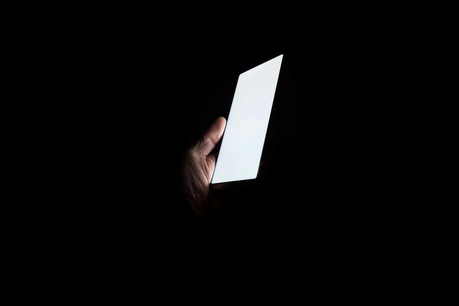 A hand holding a phone with a blank, glowing screen in the dark