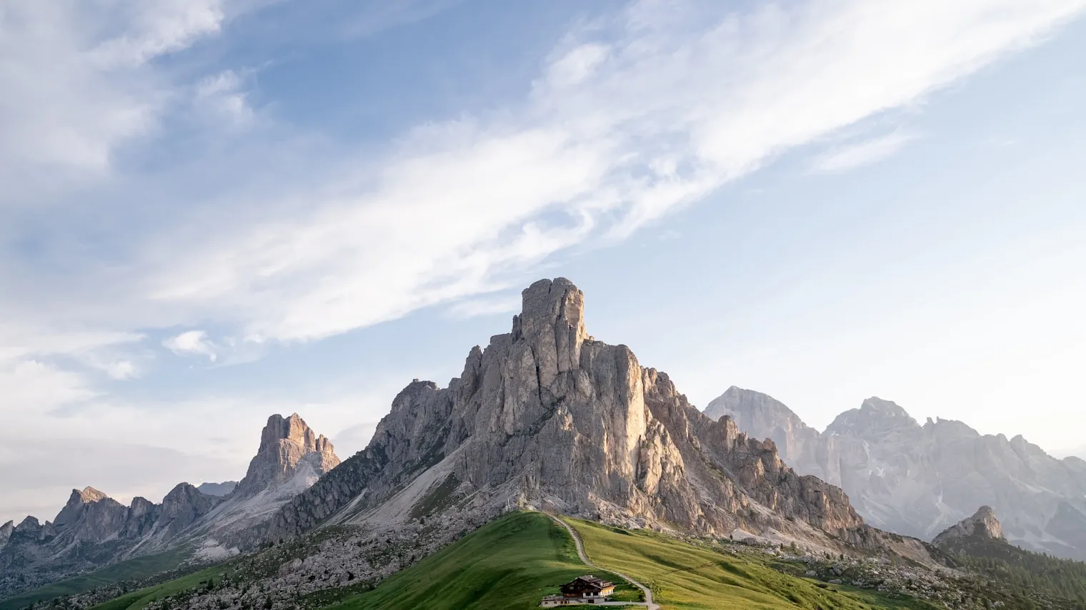 Green alpine meadow and a mountain hut below the pale rock towers of the Dolomites at sunset