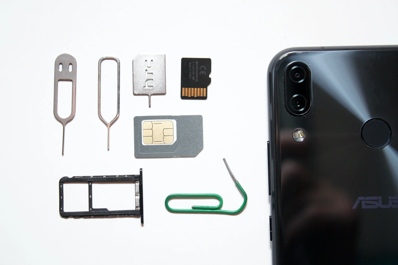 Physical SIM card, ejector pins and SIM tray laid out next to a smartphone