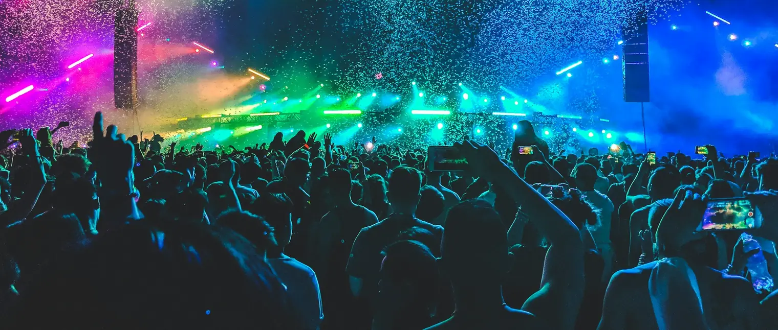 A dense festival crowd in front of a lit stage, with several phones held up above people's heads filming