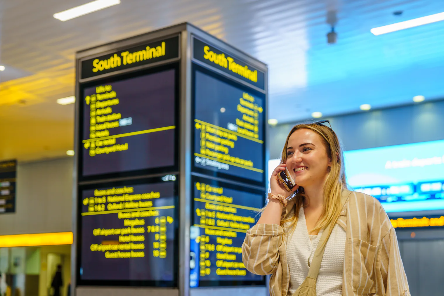 A traveller talking on her phone in an airport terminal beside the flight information boards