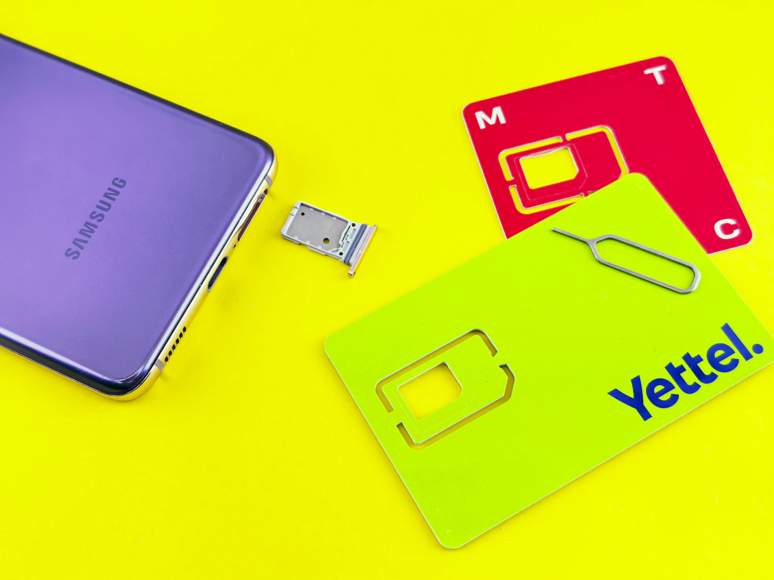Un móvil con la bandeja SIM extraída, junto a dos tarjetas SIM de plástico y la aguja de expulsión
