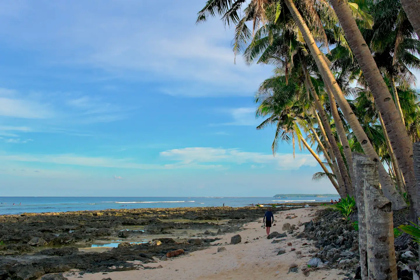 Surfer walking along the reef-fringed beach at Tuazon Point, a surf spot on Siargao Island, Philippines