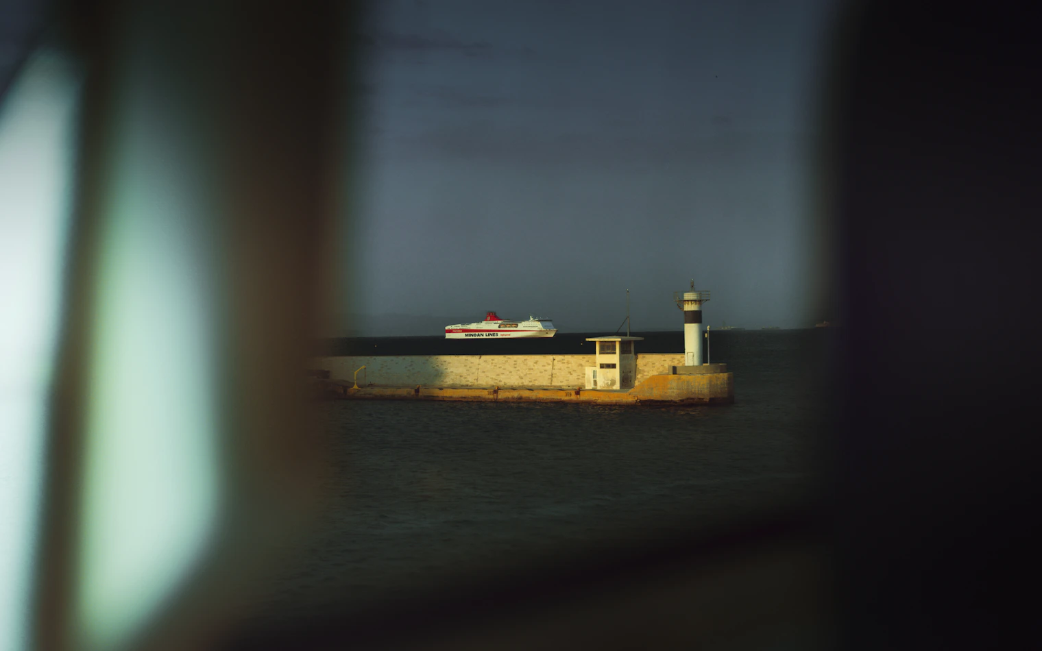 A cruise ship and a lighthouse seen from a harbour on a Mediterranean morning