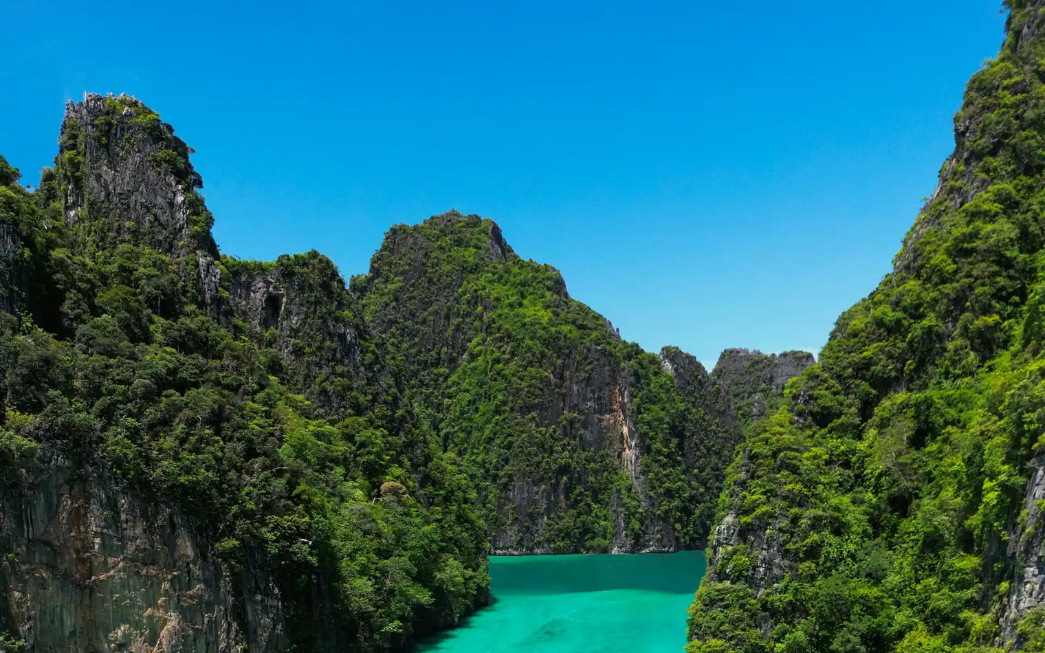 Long-tail boats on the turquoise water of Pileh Lagoon, surrounded by limestone cliffs, Koh Phi Phi Leh, Thailand
