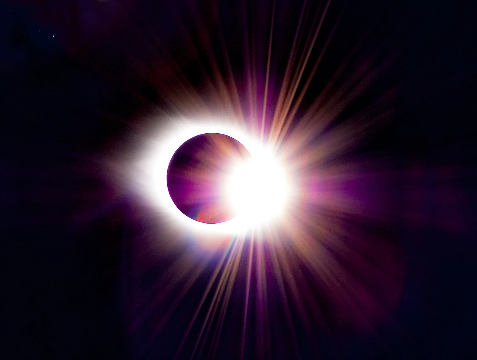 The sun's corona blazing around the dark disc of the moon during totality, against a black sky
