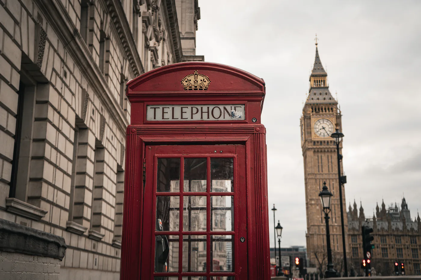 A classic red telephone box in Westminster, London, with Big Ben's clock tower rising behind it
