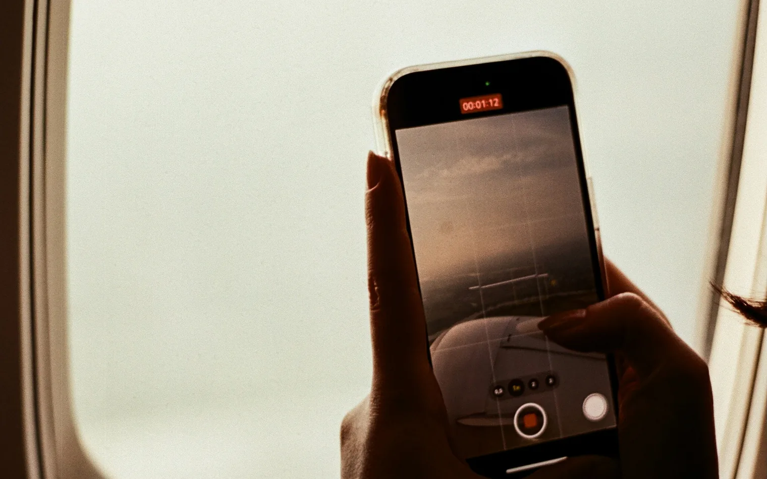 Traveler holding a smartphone next to an airplane window shortly before landing